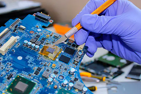 Conserto de notebook com técnico realizando manutenção na placa-mãe usando ferramenta de precisão em bancada de eletrônica