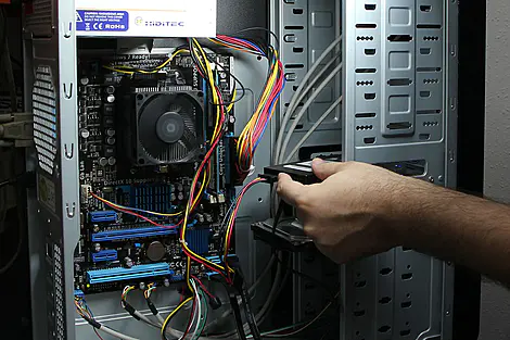 Reparação de computadores: técnico instalando disco rígido em desktop aberto com componentes internos visíveis e cabos conectados